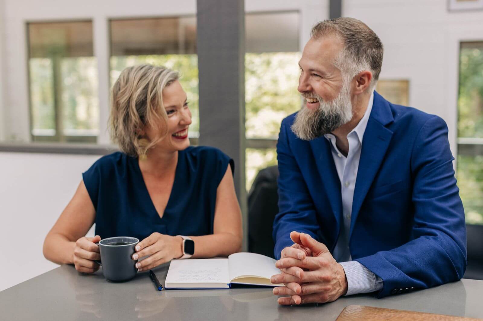 a man and woman sitting at a conference table, smiling and laughing