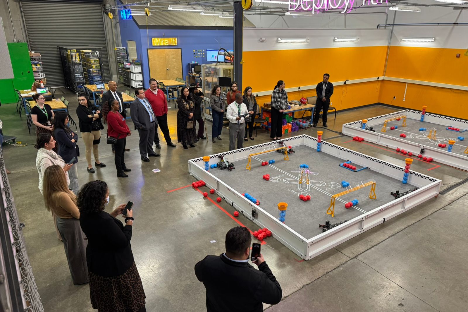 Group of adults standing around indoor robotics arena with equipment and practice fields